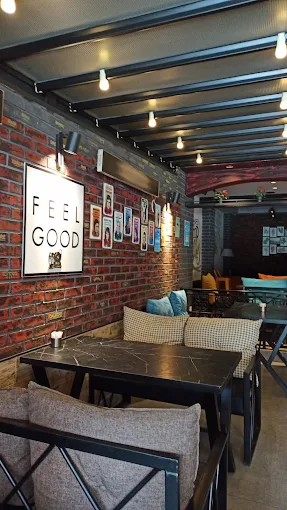 OLAFF iç mekan — tuğla duvarda FEEL GOOD tablosu, marmerimsi masalar